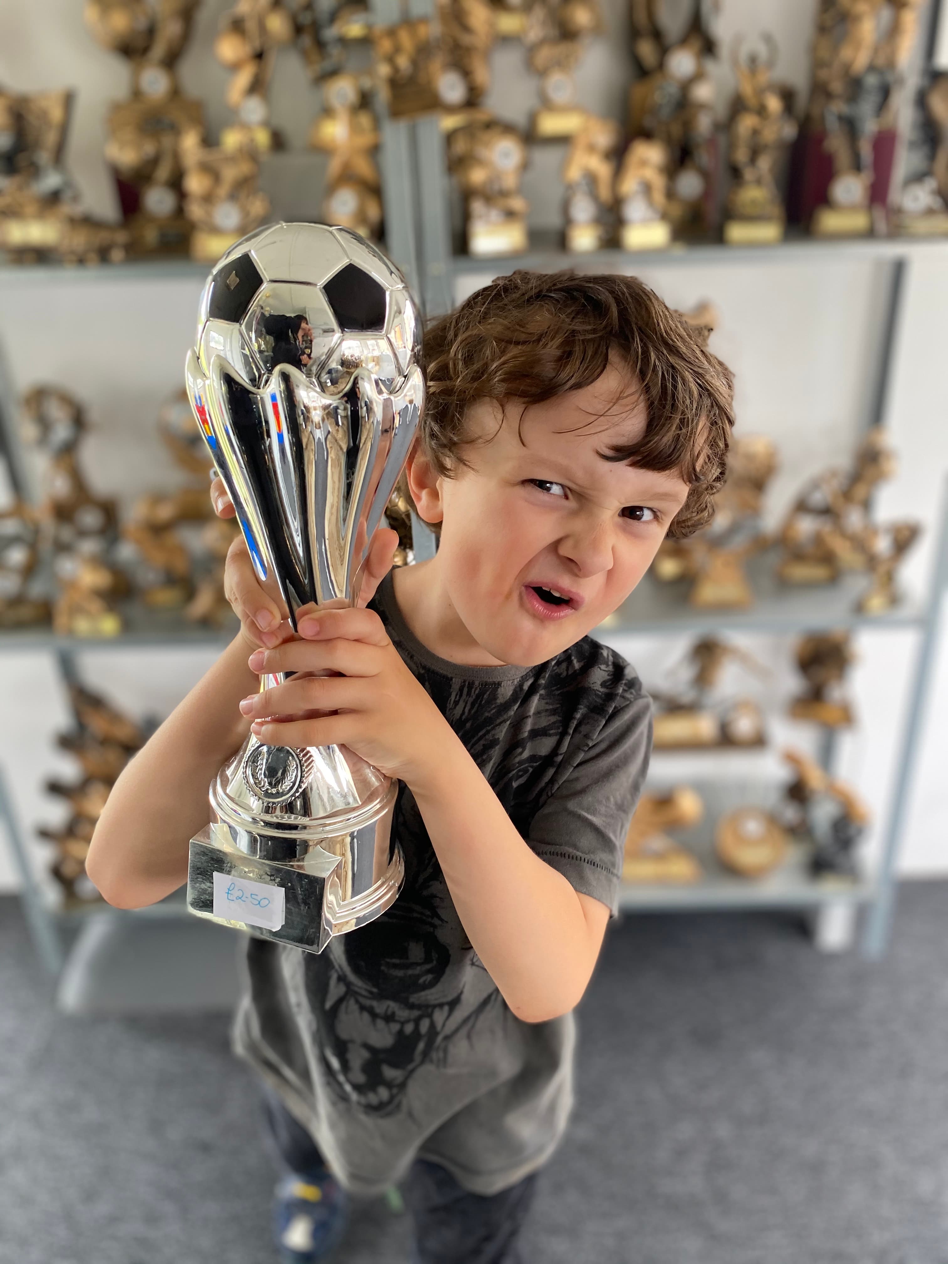 Boy holding a silver football trophy in the Hewitt's Trophies showroom